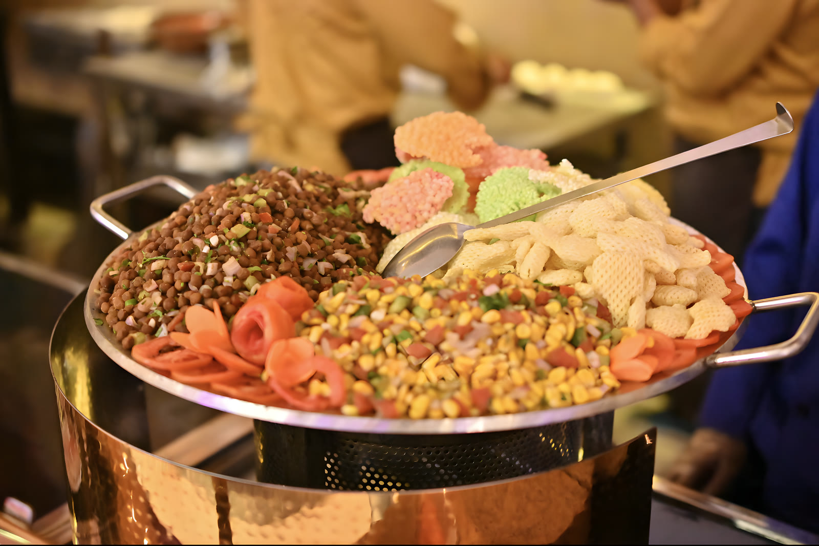 A copper pan of chaat: sprouts, corn, carrot and papdi, with a serving spoon