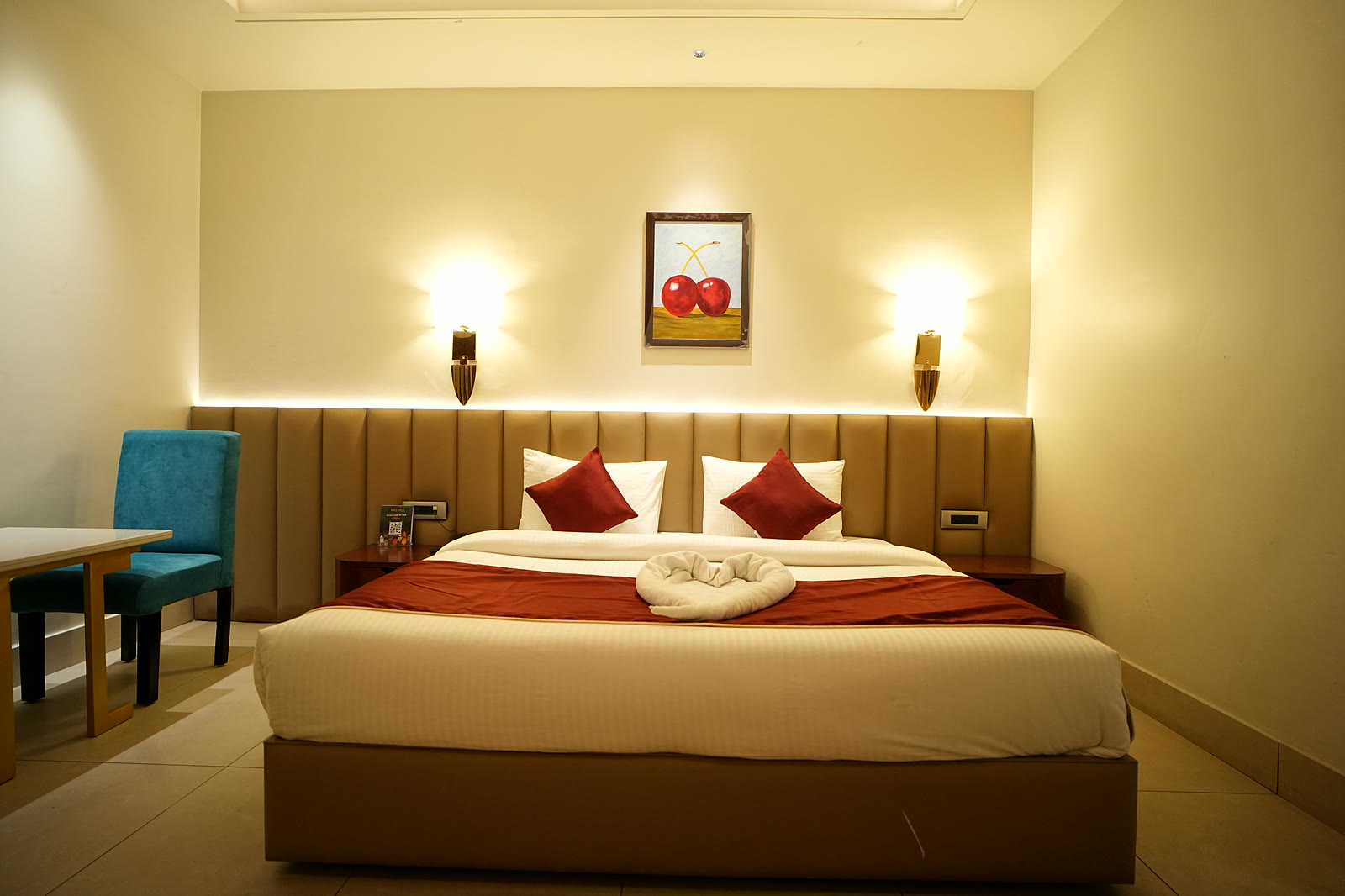 A bed with red cushions under a painting of two cherries