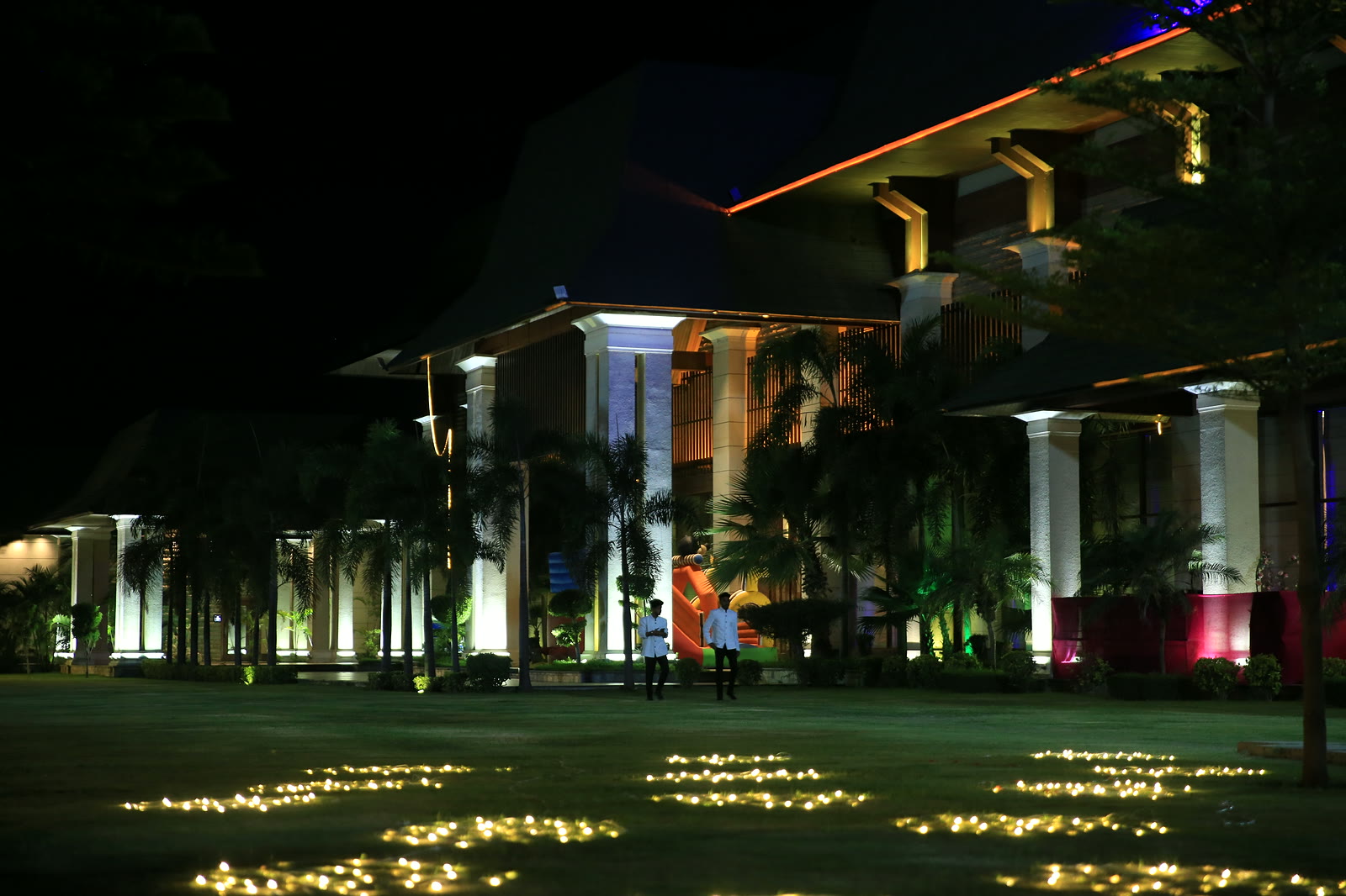 Majestic Grand at night: lit columns and palms, guests on the lawn among pools of fairy lights