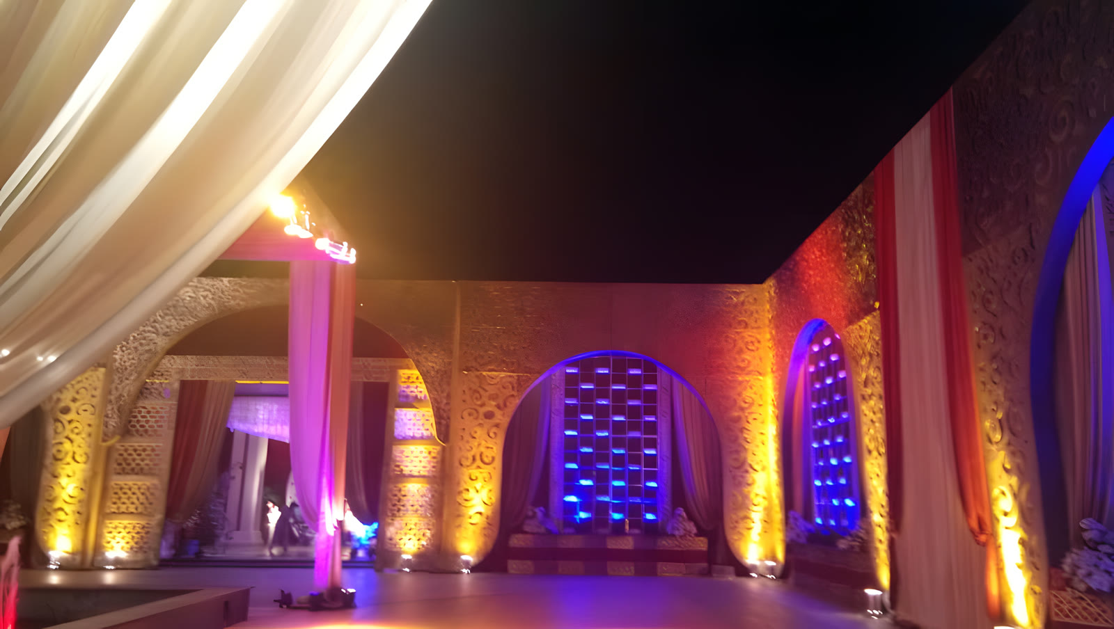 The hall lit in violet and amber, with arched backdrops